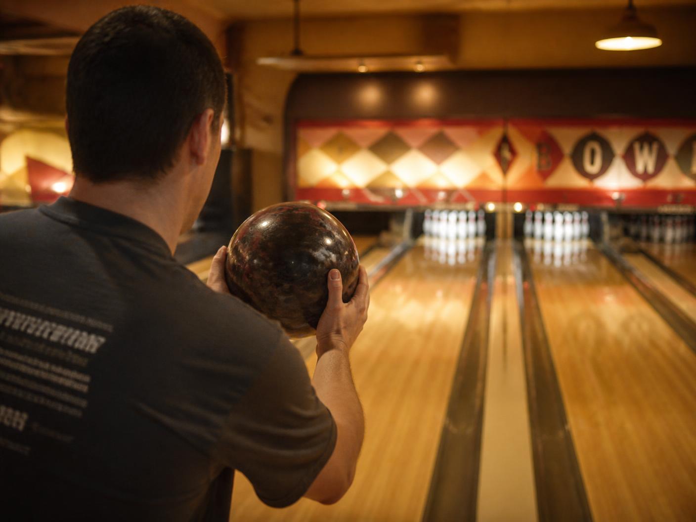 Bowling league player holding a bowling ball at the approach, lanes and pins lit up ahead