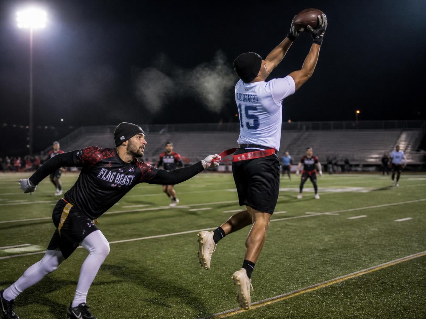 Flag football receiver catching a pass under stadium lights as a defender reaches for the flag belt