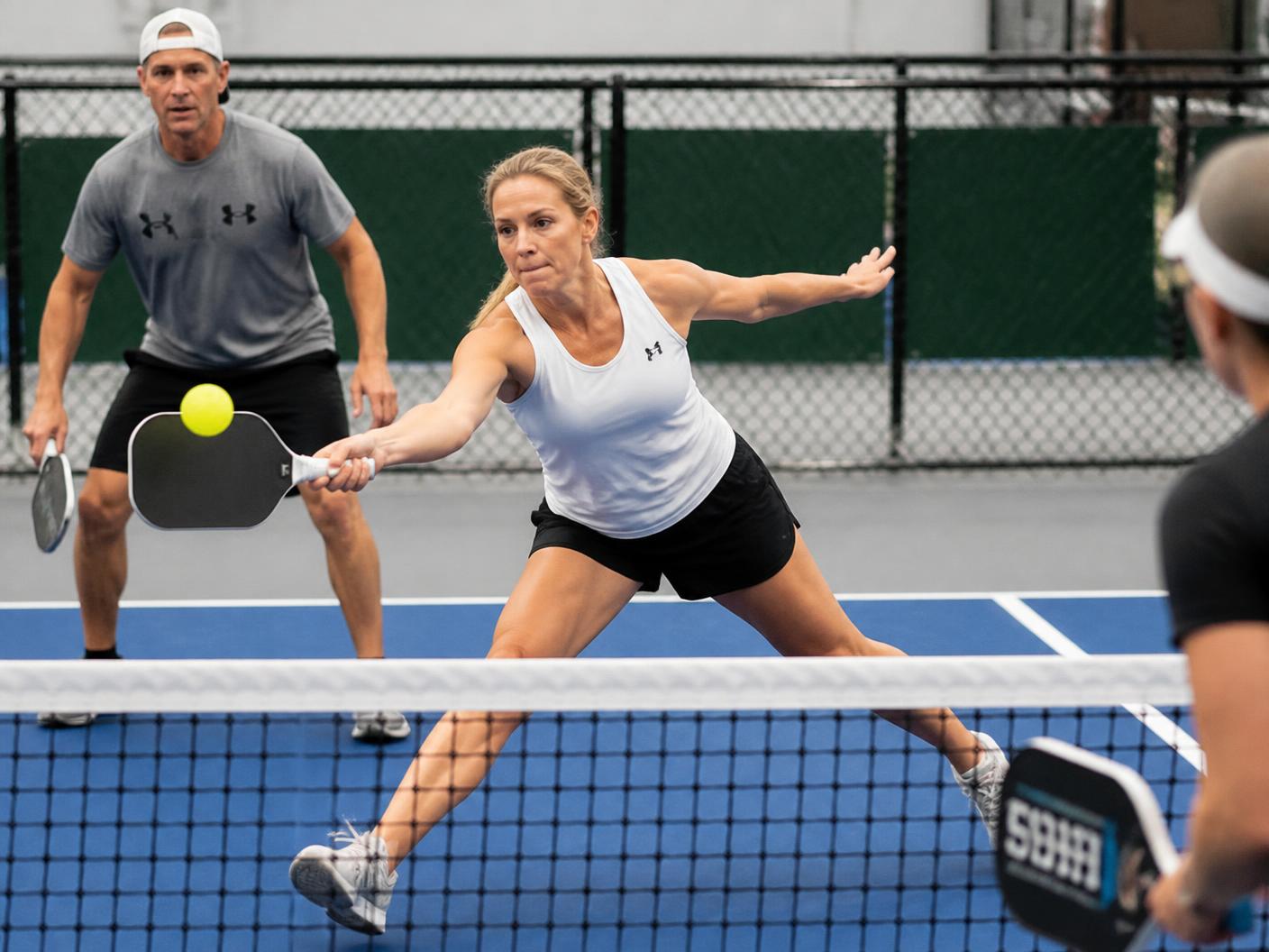 Pickleball doubles players lunging for a volley at the net on an indoor court